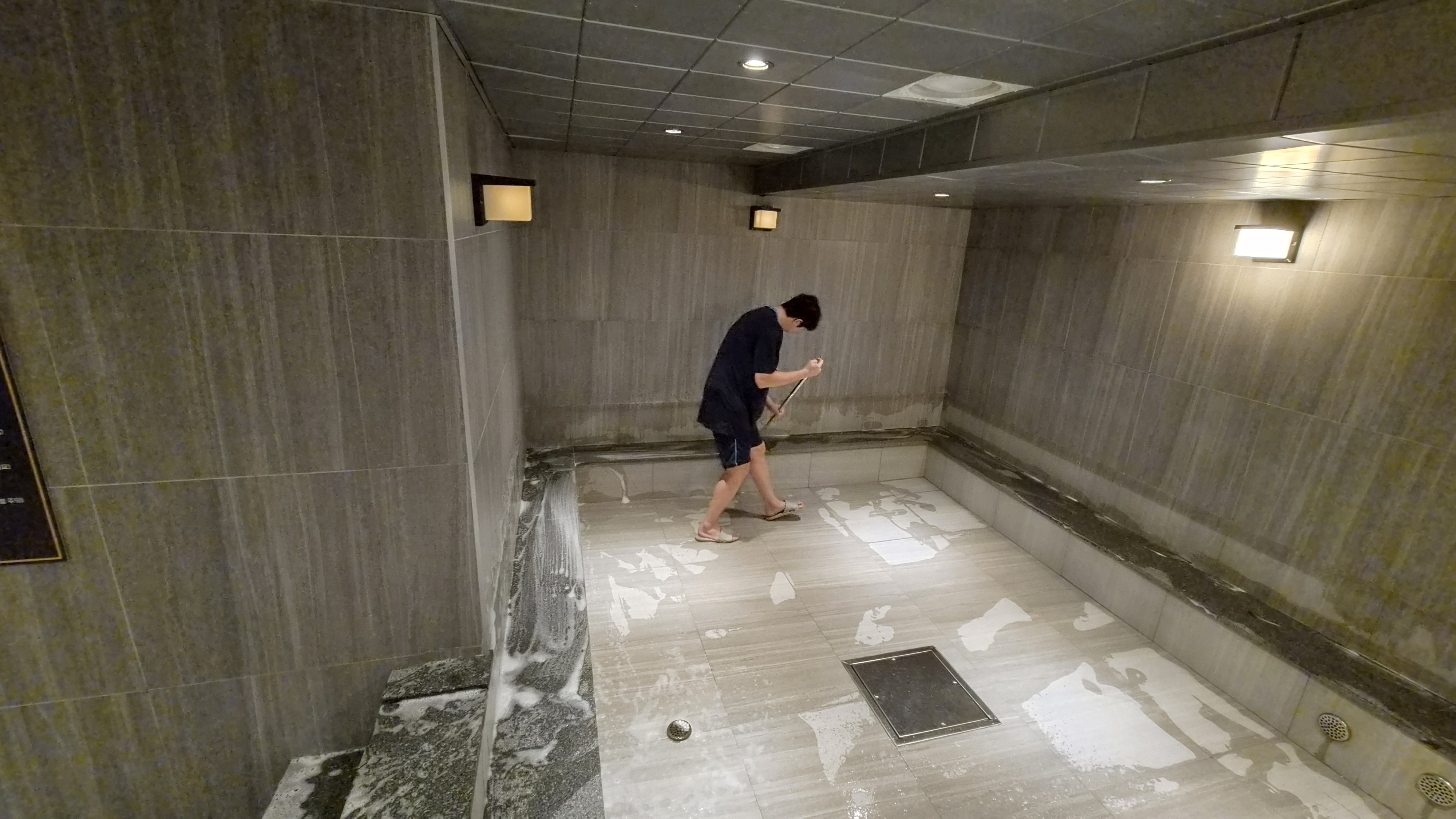 긴 손도구로 사우나 바닥을 세척하는 작업자